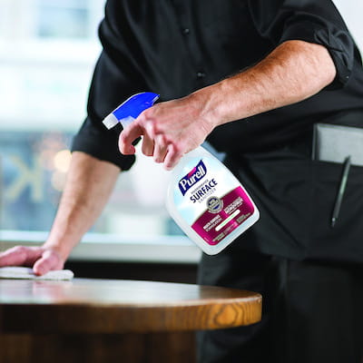 Restaurant worker cleaning table with PURELL Foodservice Surface Sanitizer