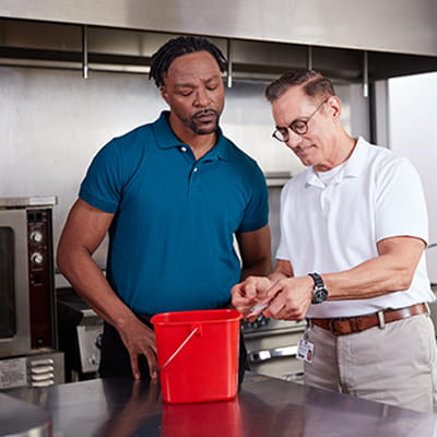 Health inspector and restaurant manager in kitchen, with red cleaning bucket
