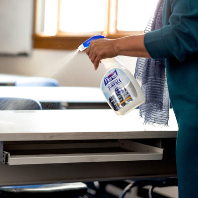 Teacher spraying classroom desk with PURELL surface disinfectant