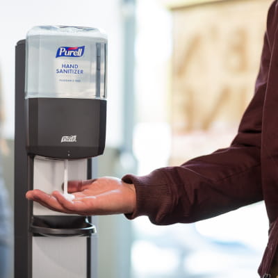 Person's hand reaching for a pump of PURELL hand sanitizer from a PURELL ES8 dispenser