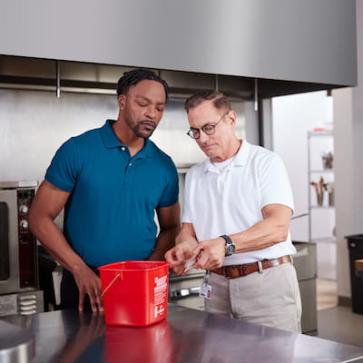 Foodservice public health inspector training employee on red bucket best practices in the back of house environment