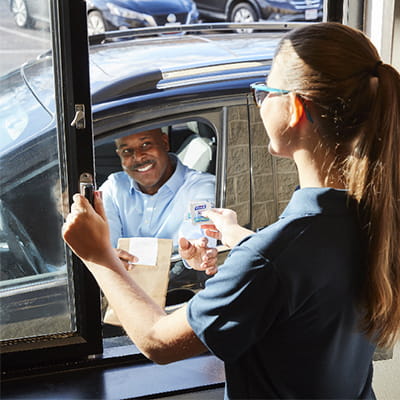 Drive-thru restaurant worker hands drive-up customer a PURELL hand sanitizing wipe